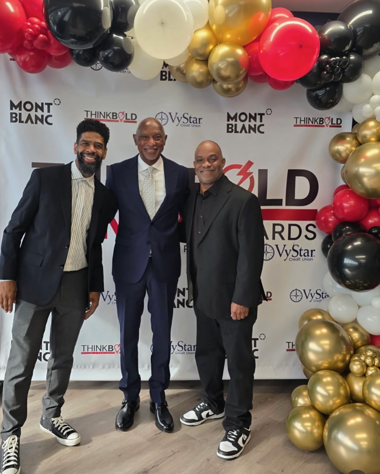 Troy and Mo on the red carpet at the Think Bold Awards, with a guest between them in front of the step-and-repeat backdrop