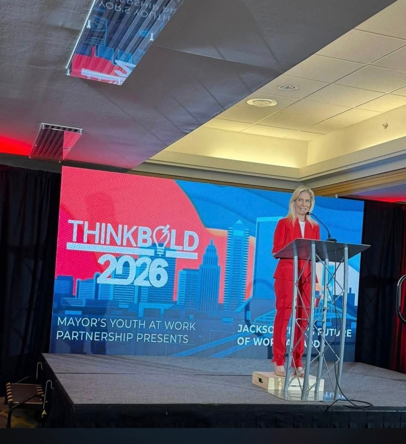 A speaker at the podium on the ThinkBold 2026 main stage, presented by the Mayor's Youth at Work Partnership