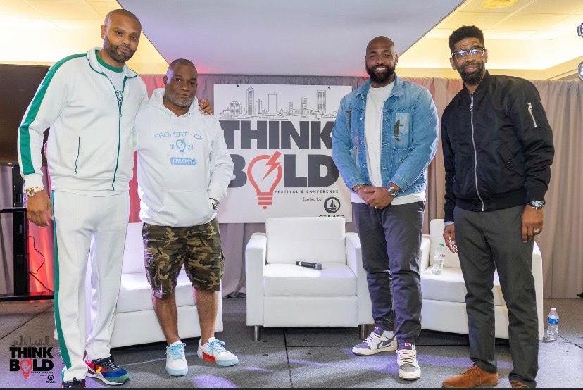 Troy and Mo with two guests standing on the Think Bold Festival set among the white armchairs